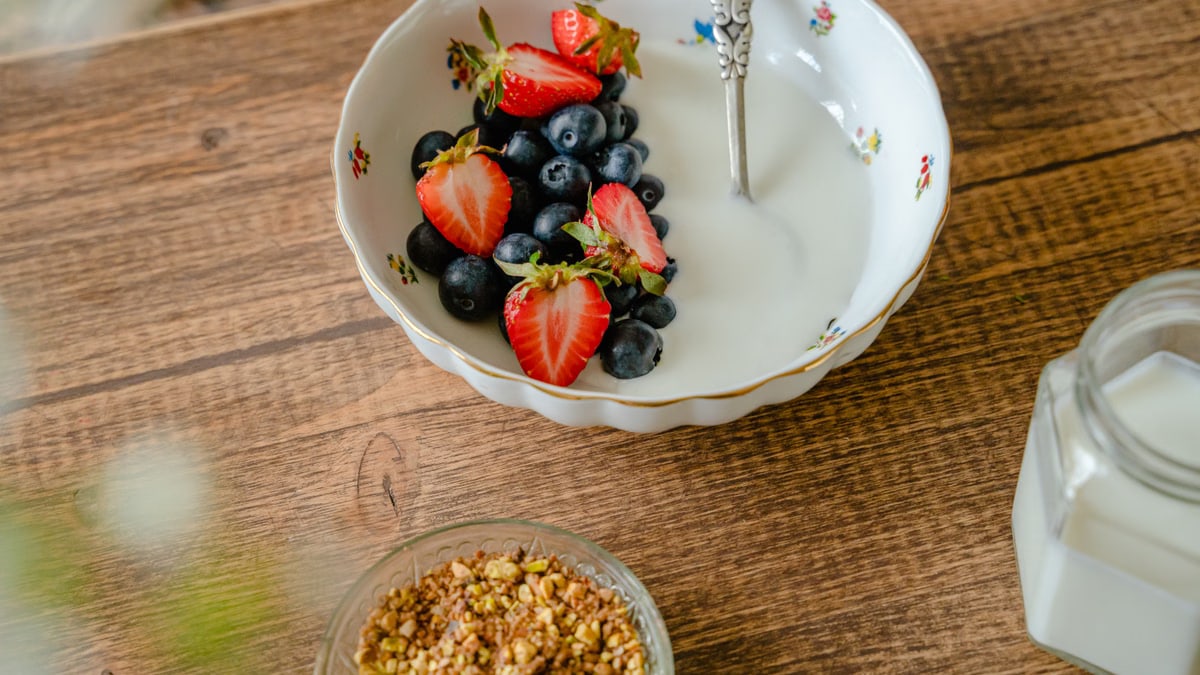 Top view of a breakfast bowl featuring strawberries, blueberries, and yogurt on a wooden table.